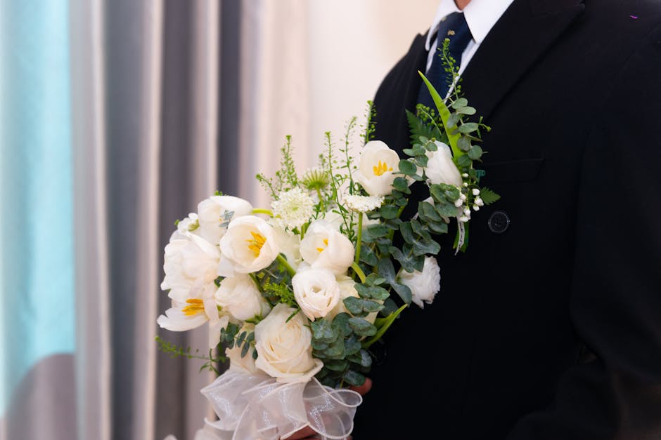 A florist from Tolworth Florist is holding a floral gift arrangement composed of white flowers, including lisianthus, roses, and tulips, accented with green foliage such as eucalyptus and fern-like sp