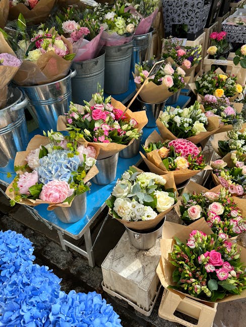 A vibrant display of floral arrangements at Tolworth Florist, showcasing bouquets and potted plants featuring roses, hydrangeas, lisianthus, and carnations in shades of pink, white, and green. The flo
